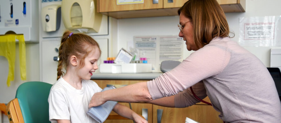 School of Medicine building with large windows and a wooden deck, bordered by a glass railing. A tree stands near the building under a clear blue sky