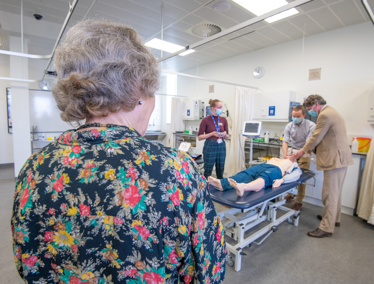 Group of four people in clinical setting. Two of the people are interacting with a Resuscitation Anne in a simulation, while the other two people look on.