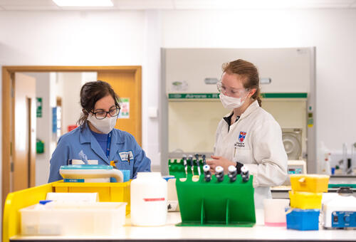 Students wearing face-coverings during labwork, University of St student and professor in lab